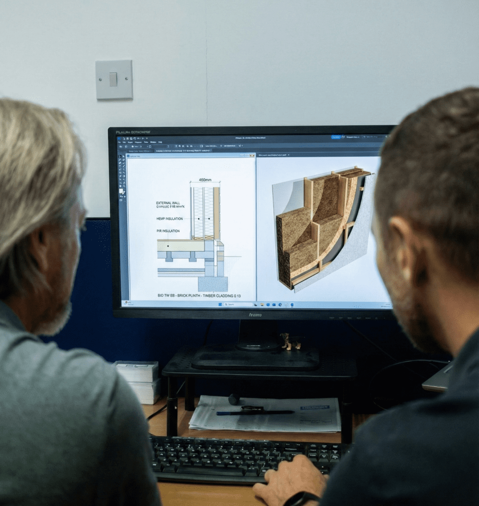 Two men examining a computer screen displaying a wood design, engaged in discussion about the project.